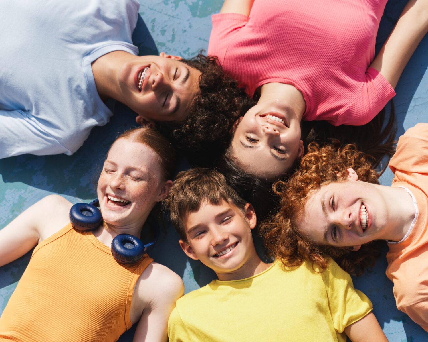 Portrait of smiling teenagers boys and girls lying on the sportive field at daytime, looking at camera. Summer time, lifestyle, friendship concept